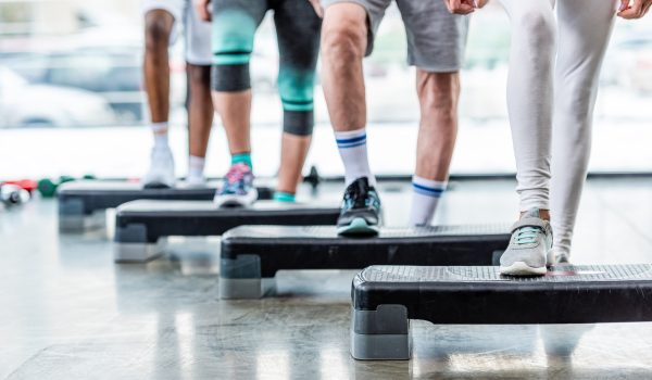 cropped image of sportspeople doing exercise on step platforms at gym