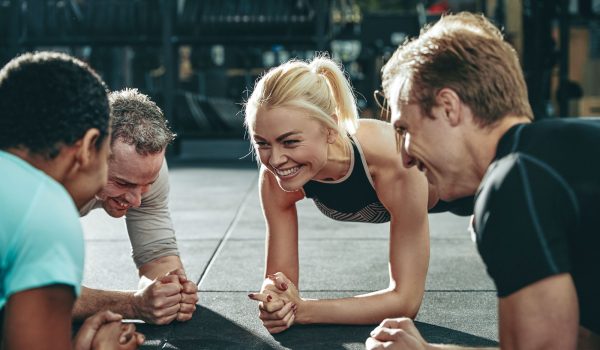 Diverse group of smiling friends in sportswear planking together on a gym floor during a workout session